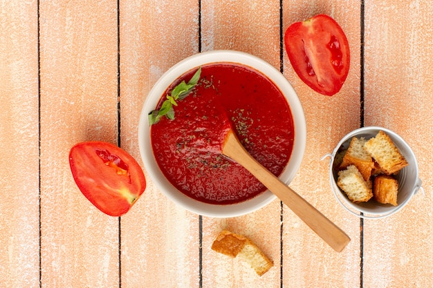 Top view tomato soup with greens along with red tomatoes on rustic table, soup food meal dinner vegetable