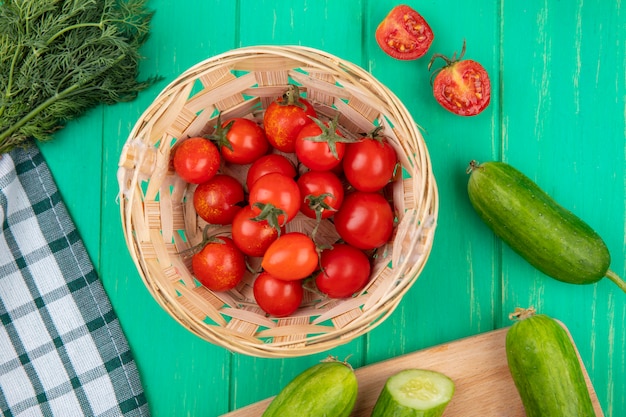 Top view of tomatoes in basket and cucumber dill around on green surface