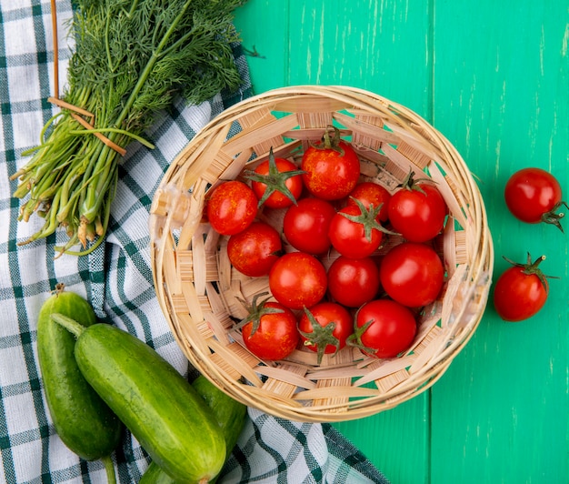 Vista superiore della merce nel carrello dei pomodori e aneto del cetriolo intorno sul panno del plaid e sulla superficie verde