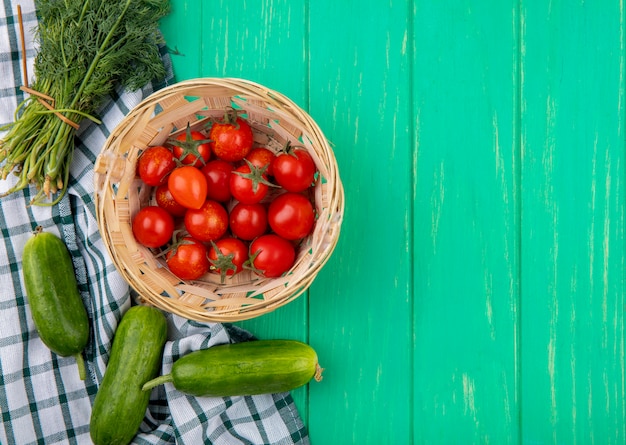 Взгляд сверху томатов в корзине и укропе огурца вокруг на ткани пледа и зеленой поверхности