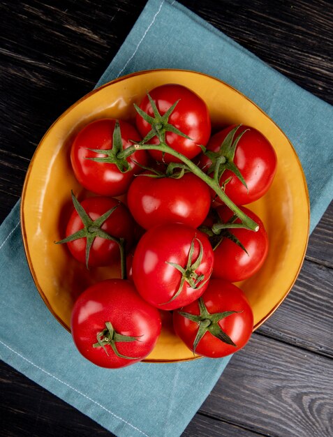 Top view of tomatoes in bowl on blue cloth and wooden surface