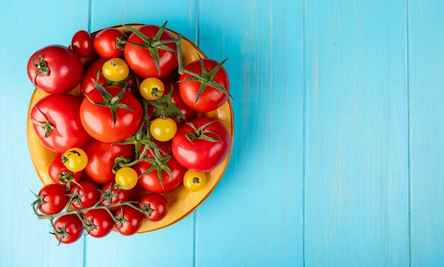 Top view of tomatoes in bowl on left side and blue surface with copy space