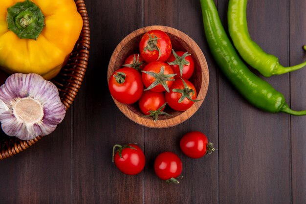 Top view of tomatoes in bowl and pepper garlic in basket on wooden surface