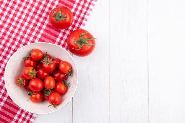 Top view of tomatoes in bowl and on plaid cloth on wooden surface