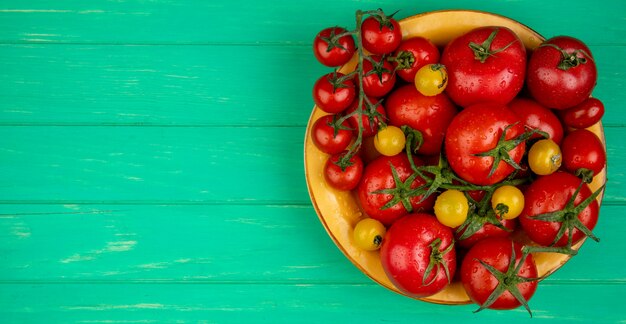 Top view of tomatoes in bowl on right side and green surface with copy space