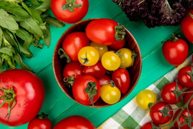 Top view of tomatoes in bowl with green mint leaves and basil on green