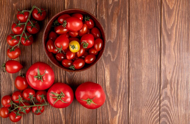 Top view of tomatoes in bowl with other ones on left side and wooden surface with copy space