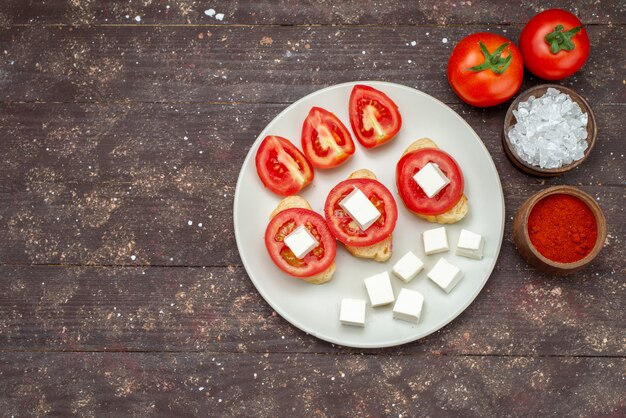 Top view tomatoes and cheese inside white plate with seasonings on the brown wooden rustic background food vegetable salad photo