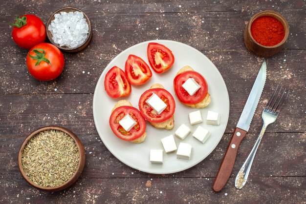 Top view tomatoes and cheese inside white plate with seasonings on the brown wooden rustic background food vegetable salad