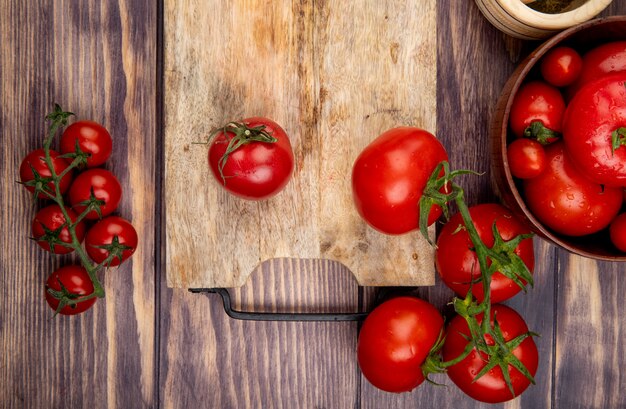 Top view of tomatoes on cutting board with other ones on wooden surface