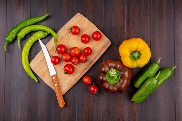 Vista superiore di pomodori e coltello sul tagliere con peperoni e cetrioli intorno su superficie di legno