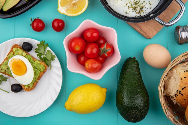 Top view of tomatoes on a pink bowl with toasted bread on a white plate on blue surface