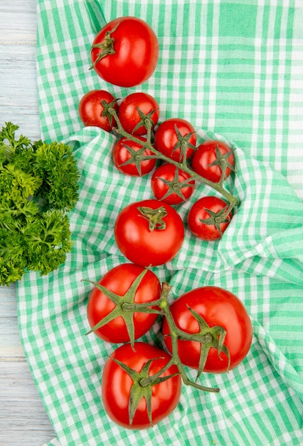 Top view of tomatoes on plaid cloth with coriander on wooden surface