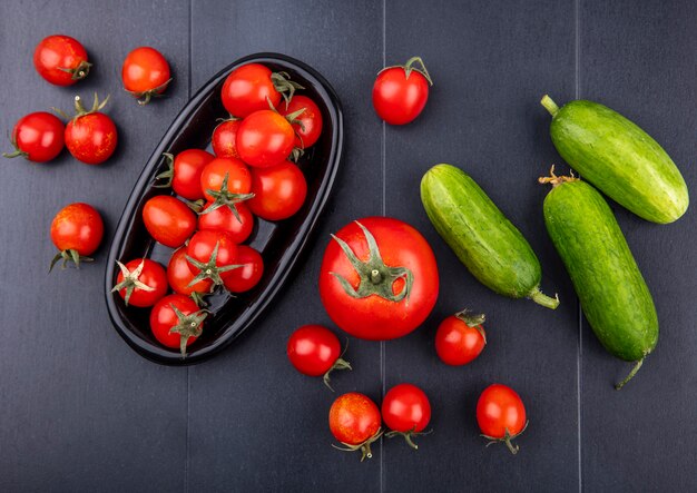 Top view of tomatoes in plate with cucumbers on black surface