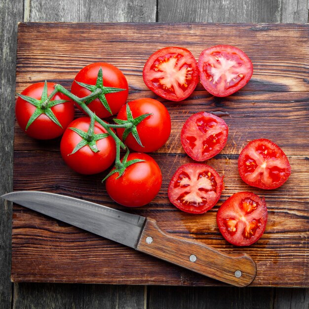 Top view tomatoes and slices on a wooden cutting board with knife on dark wooden background.