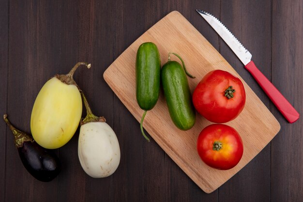 木製の背景のまな板にキュウリナスとナイフとトップビュートマト
