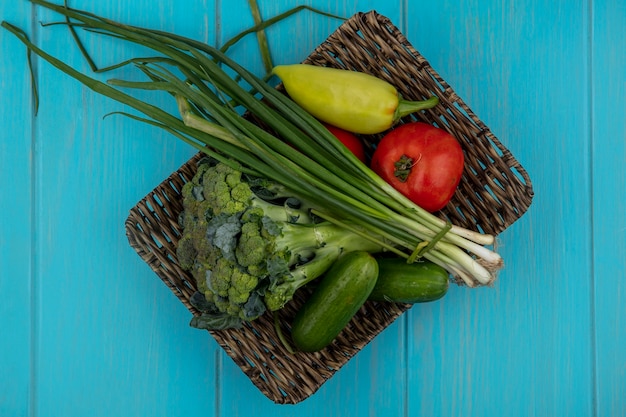 Foto gratuita vista dall'alto pomodori con cetrioli, cipolle verdi, broccoli e peperoni su un supporto su uno sfondo turchese