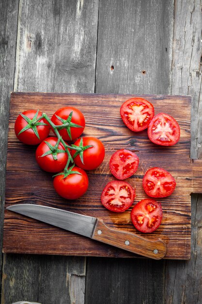 Top view tomatoes with slices in wooden cutting board with knife on dark wooden background. vertical