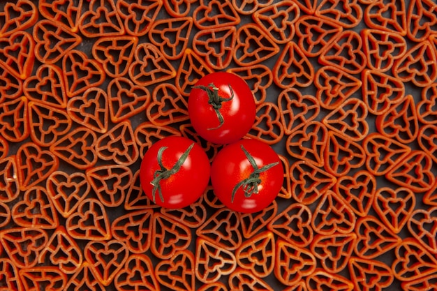 Foto gratuita tometoes vista dall'alto su pasta italiana di cuori rossi sul tavolo scuro