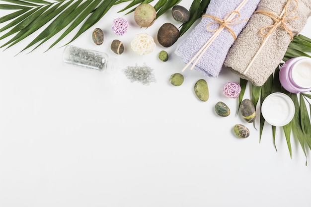 Top view of towels; moisturizing cream; spa stones and leaves on white surface