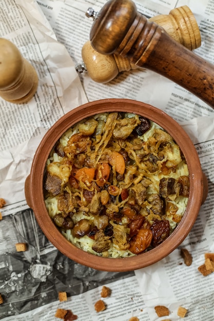 Top view a traditional azerbaijani dish pilaf with meat and fried dried fruits with onions in a clay dish on a newspaper