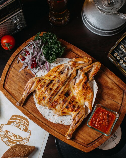 Top view of traditional caucasian cuisine of grilled chicken tabaka with red onion herbs and tomato sauce adjika