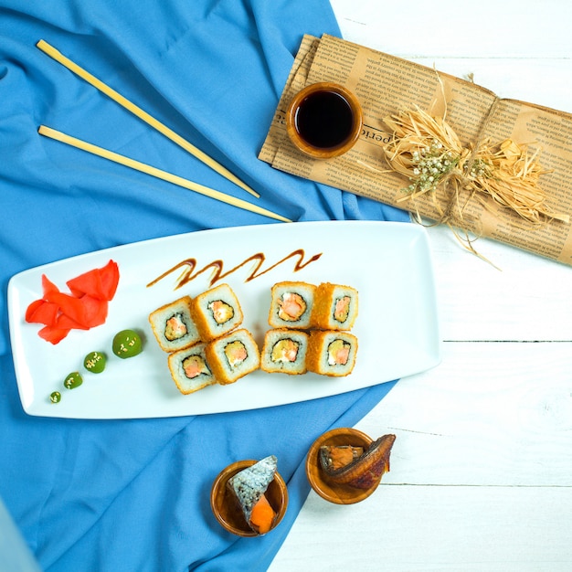 Foto gratuita vista superiore del rotolo di sushi giapponese tradizionale di cucina con avocado di salmone e crema di formaggio su blu e bianco