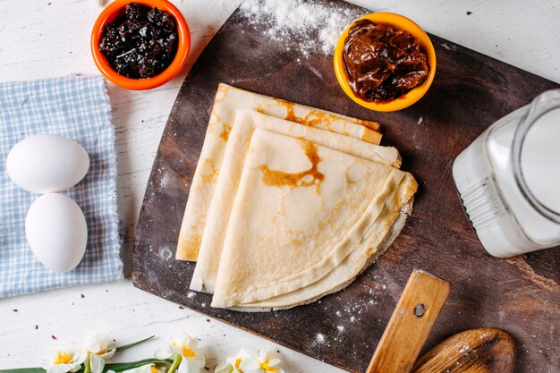 Top view of traditional russian breakfast pancake with jam sauce and milk on a wooden cutting board