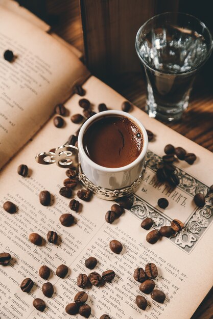Top view traditional turkish coffee with coffee beans on an open book with a glass of water