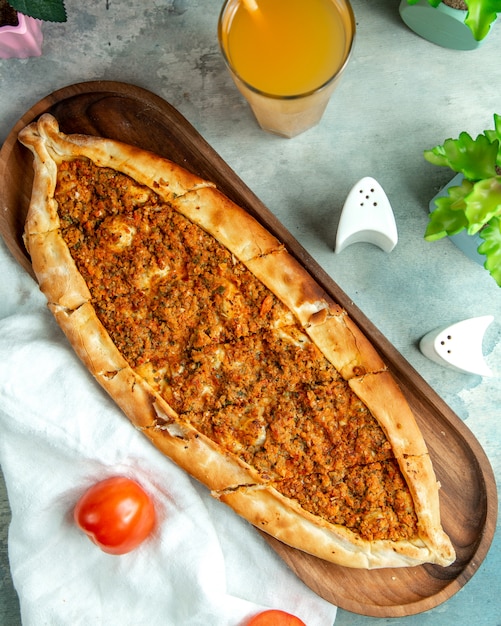 Top view traditional turkish dish meat pide on a tray with tomatoes and juice