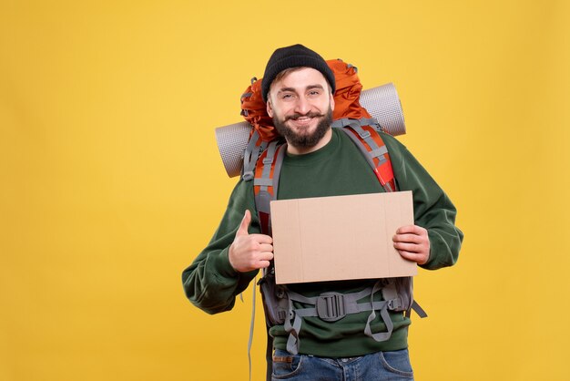 Top view of travel concept with smiling young guy with packpack holding free space for writing making ok gesture