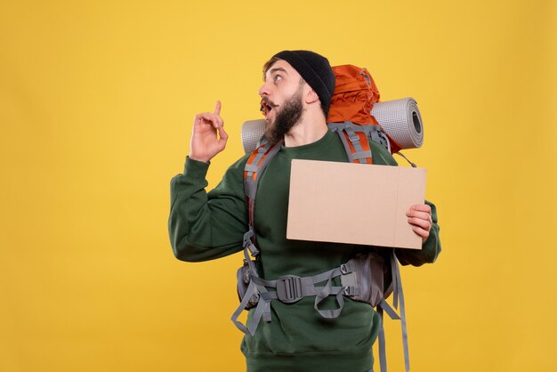 Top view of travel concept with young guy with packpack and holding free space for writing pointing up