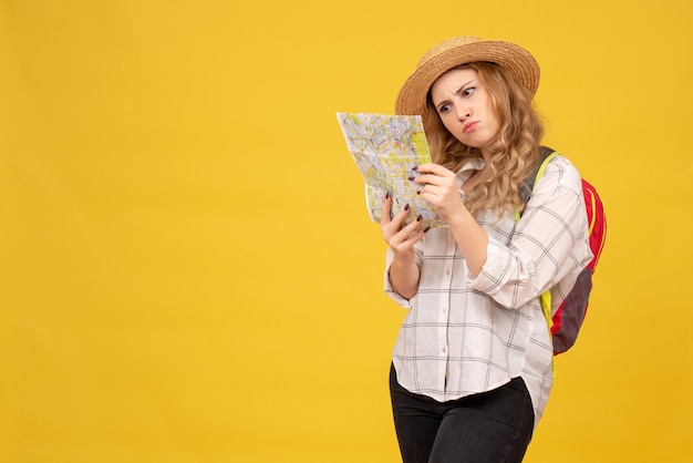 Вид сверху путешествующей девушки в шляпе и рюкзаке, смотрящей на карту на желтом