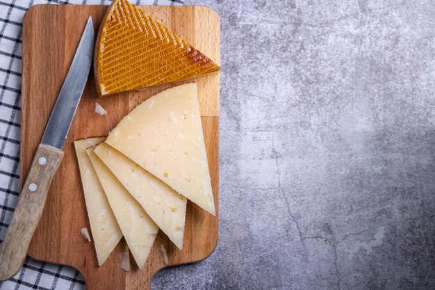 Вид сверху на треугольные кусочки вяленого сыра Манчего и острый нож на деревянной доске