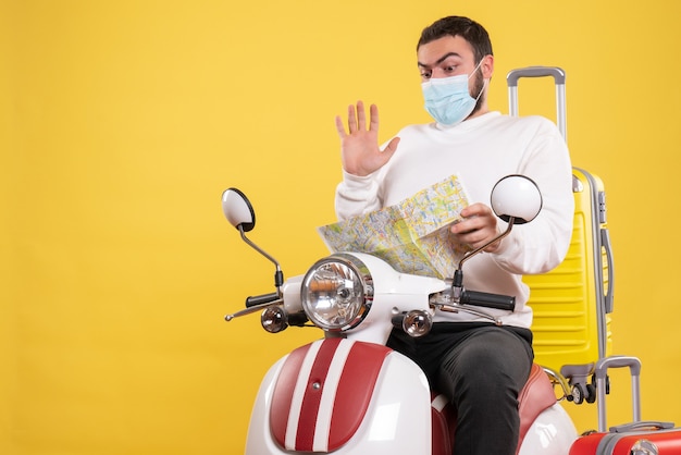 그것에 노란색 가방과 함께 오토바이에 앉아지도를 들고 의료 마스크에 혼란스러운 남자와 여행 개념의 상위 뷰