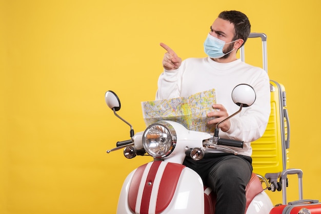 Vista dall'alto del concetto di viaggio con un ragazzo curioso in maschera medica seduto su una moto con valigia gialla su di essa e con in mano la mappa