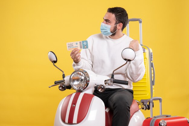Вид сверху на концепцию поездки с молодым любопытным парнем в медицинской маске, сидящим на мотоцикле с желтым чемоданом и держащим билет