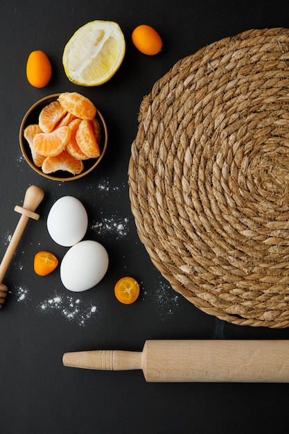 Free photo top view of trivet with egg lemon half tangerine slices kumquat with honey dipper and rolling pin on black background