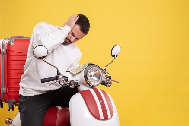 Top view of troubled man sitting on motorcycle with suitcase on it holding map suffering from headache on isolated yellow background