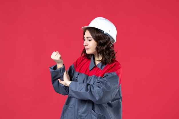 ヘルメットと制服を着て、孤立した赤い背景の上の手の痛みに苦しんでいる厄介な女性ビルダーの上面図