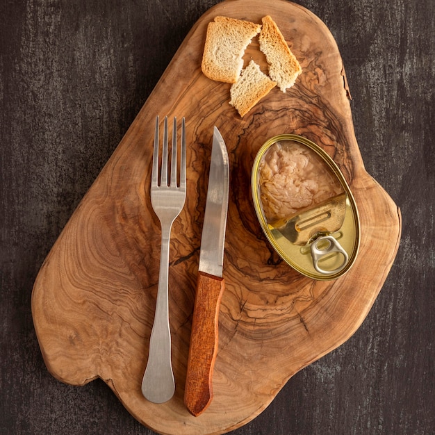 Top view tuna can on wooden board with cutlery