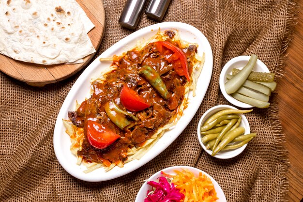 Top view of turkish beef kebab garnished with spicy tomato sauce served with pickles