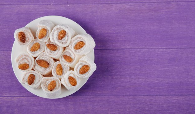 Top view of turkish delights rahat lokum on a white plate on purple wooden surface with copy space