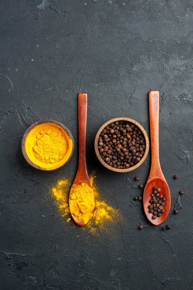 Free Photo top view turmeric black pepper in small bowls in wooden spoons on black table