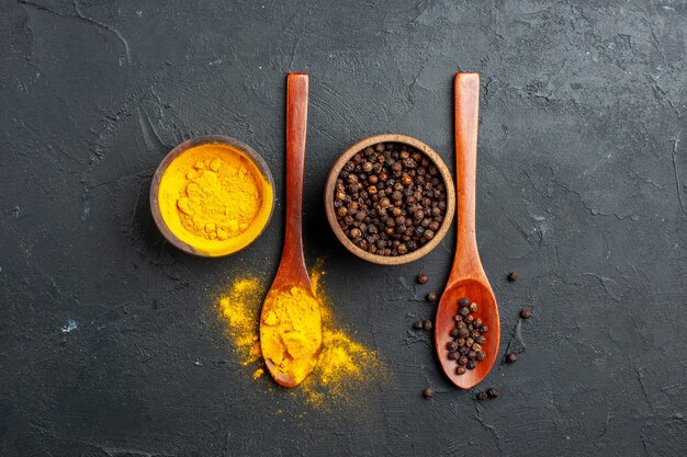 Top view turmeric black pepper in small bowls in wooden spoons on dark table free space