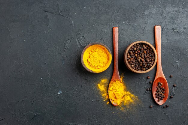 Top view turmeric black pepper in small bowls in wooden spoons on dark table free space