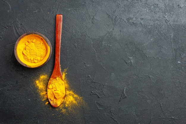 Free photo top view turmeric bowl turmeric in wooden spoon on dark table with free space