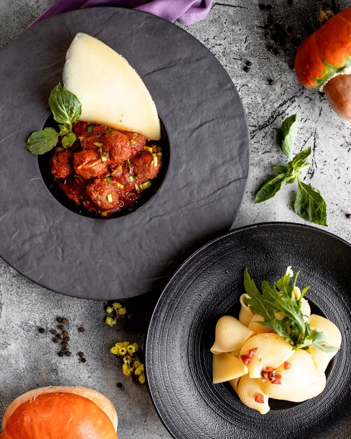 Top view of two plates with meatballs in tomato sauce and sheashells pasta