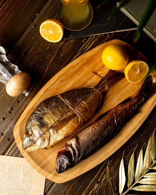 Top view of two smoked fish placed on bamboo plate with lemon halves