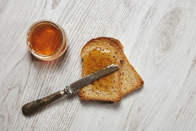 세 닦 았된 흰색 나무 테이블과 크루통에 빈티지 칼에 고립 된 장인 꿀 organig 소박한 건조 호밀 빵에서 두 토스트의 상위 뷰